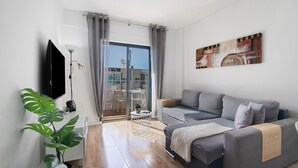 Una sala de estar moderna con un sofá gris, un televisor de pantalla plana, una planta en maceta y vistas al exterior.