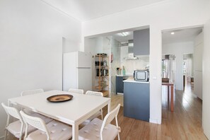 Une cuisine moderne avec des meubles blancs, un four à micro-ondes encastré et une table à manger en bois avec des chaises.