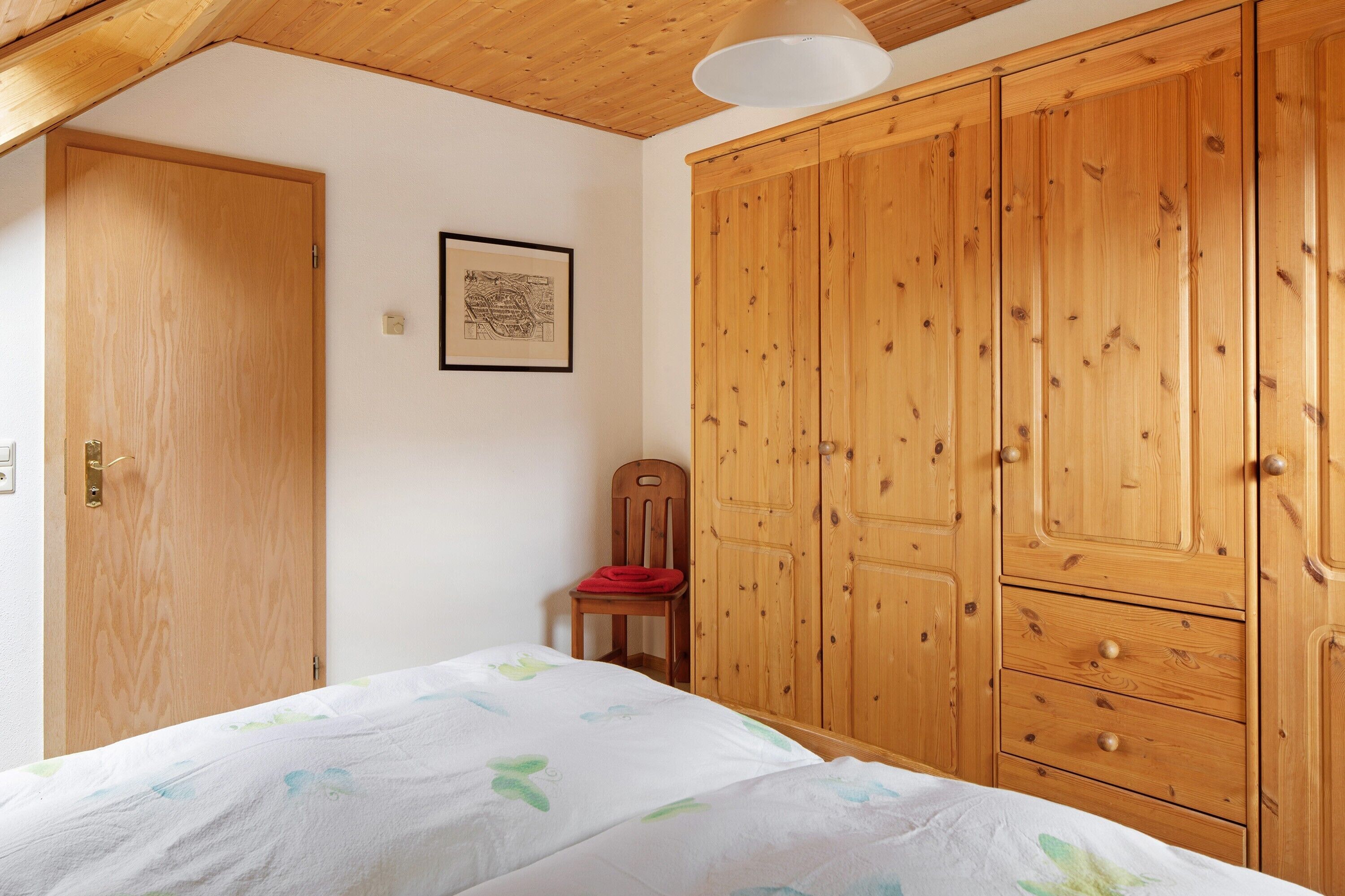 Quarto com cama, guarda-roupa de madeira e uma cadeira.