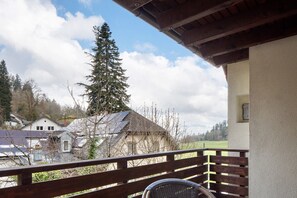Un balcon avec une balustrade en bois, une chaise en osier et une vue sur des maisons et des arbres.