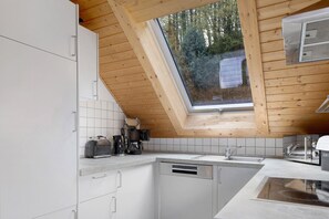 Une cuisine avec des meubles blancs, un lave-vaisselle, un évier et une fenêtre donnant sur des arbres.