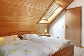 Une chambre avec un plafond en pente, des murs en bois, un puits de lumière, un lit avec une literie à motifs de feuilles, une lampe de chevet et une armoire.
