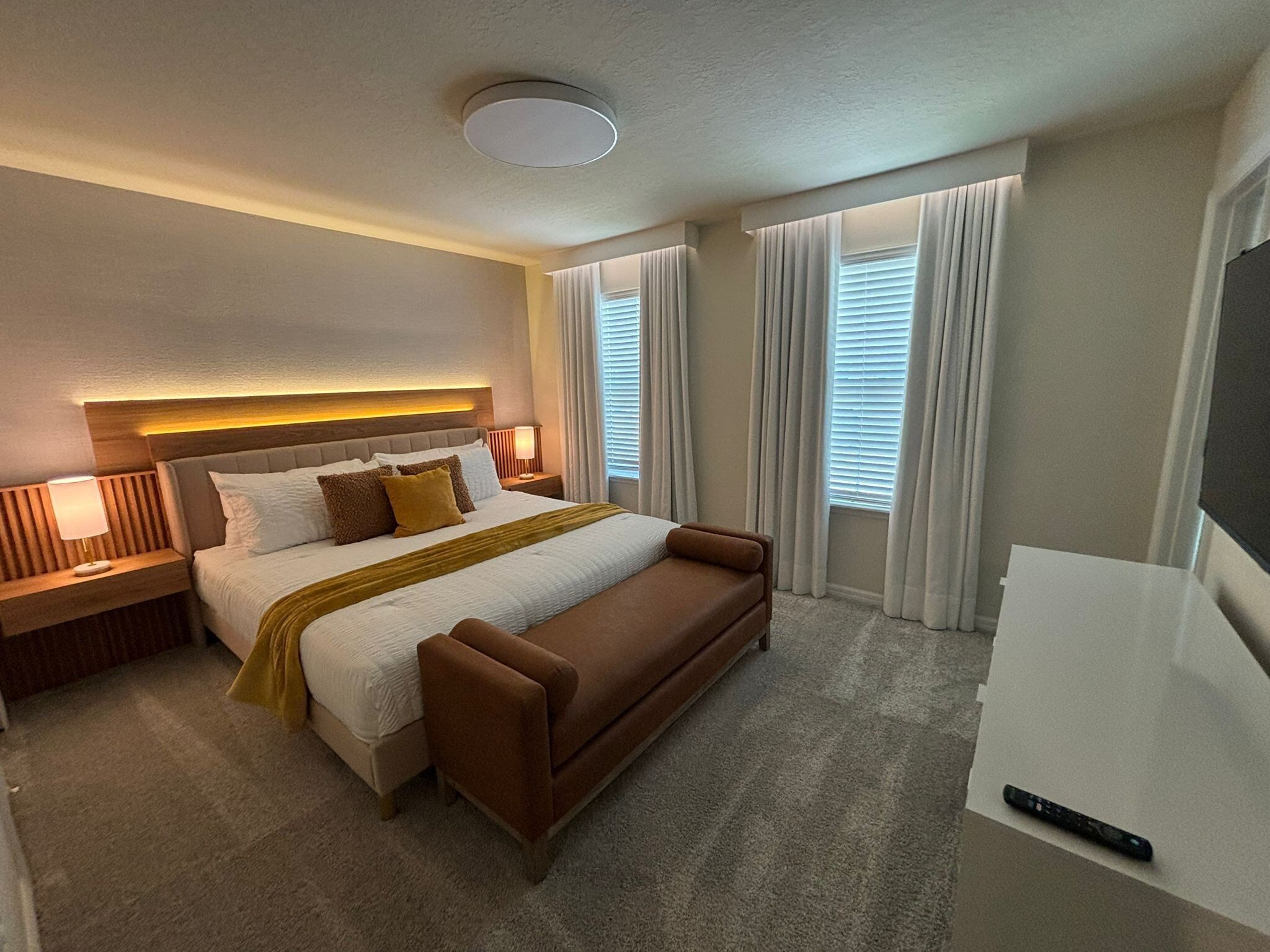 Habitación de hotel con una cama grande, una mesita de noche con lámpara, un televisor y una ventana con cortinas.