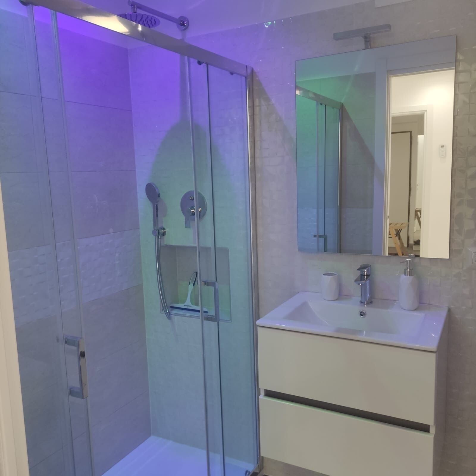 A modern bathroom with a glass-enclosed shower, a white sink with a mirror above it, and a tiled wall.
