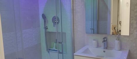 A modern bathroom with a glass-enclosed shower, a white sink with a mirror above it, and a tiled wall.