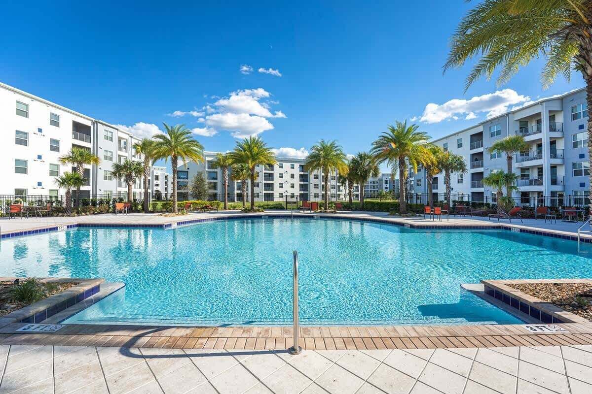 A swimming pool surrounded by palm trees and a white building with balconies.