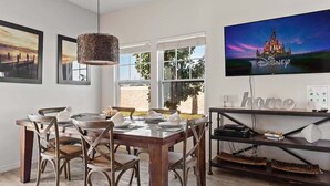 Een eetruimte met een houten tafel voor vier personen, een hanglamp en een televisie waarop het Disney-logo te zien is.