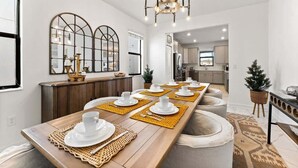 Ein Essbereich mit einem langen Holztisch, gedeckt für eine Mahlzeit, einer Chandelüster und einer Küche im Hintergrund.