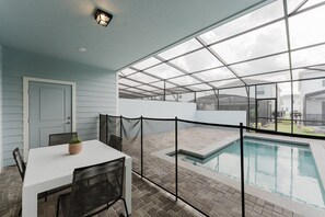 A covered patio with a pool, a table with chairs, and a door.