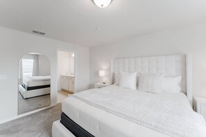 A modern, white-themed bedroom with a large bed, a nightstand, and a mirror.