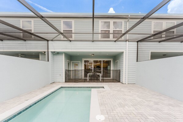 A pool area with a covered patio, a glass door entrance, and a view of the interior.