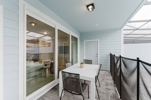 A covered patio area with a white table and chairs, a potted plant, and a glass door leading to an interior space.