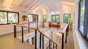 Un intérieur spacieux avec un plafond haut, de grandes fenêtres et une balustrade en verre donnant sur un niveau inférieur.