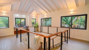 Une pièce spacieuse avec un escalier en bois, de grandes fenêtres offrant une vue sur la végétation tropicale et un design moderne.