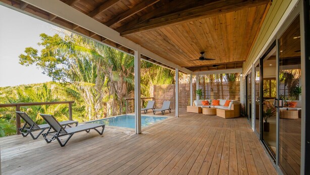 Une terrasse en bois avec une piscine, des chaises longues et un espace salon agrémenté de coussins.