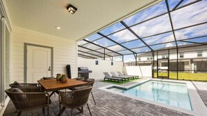 Un patio couvert avec une piscine, du mobilier d’extérieur et un espace barbecue.