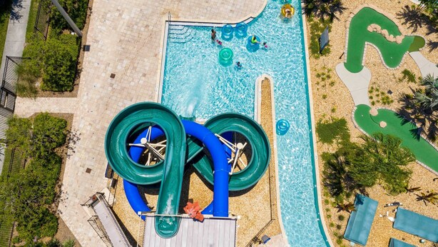 Vue aérienne d’un espace piscine avec un toboggan aquatique et un chemin verdoyant.