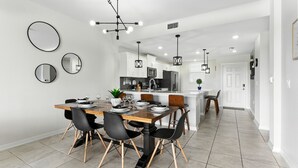 Une cuisine moderne avec des meubles blancs, un îlot central et un coin repas comprenant une table en bois et des chaises noires.