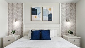 Une chambre à coucher comprenant un lit, deux tables de chevet, une tête de lit et deux appliques murales.
