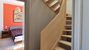 A modern interior with a wooden staircase, a bed with a colorful blanket, and a wall-mounted artwork.