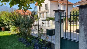 A residential area with a stone wall, a metal gate, and a paved path leading to a building with a red-tiled roof.