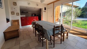 A dining area with a table and chairs, a kitchen in the background, and a sliding glass door leading to a garden.