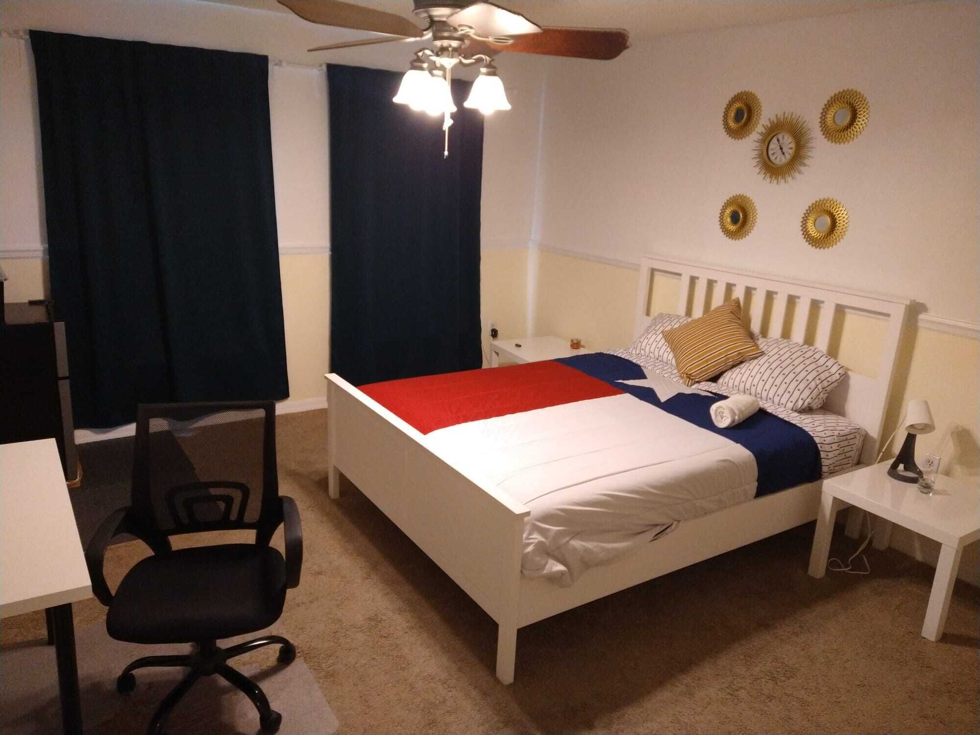 Un dormitorio ordenado con cama, escritorio, silla y ventilador de techo.