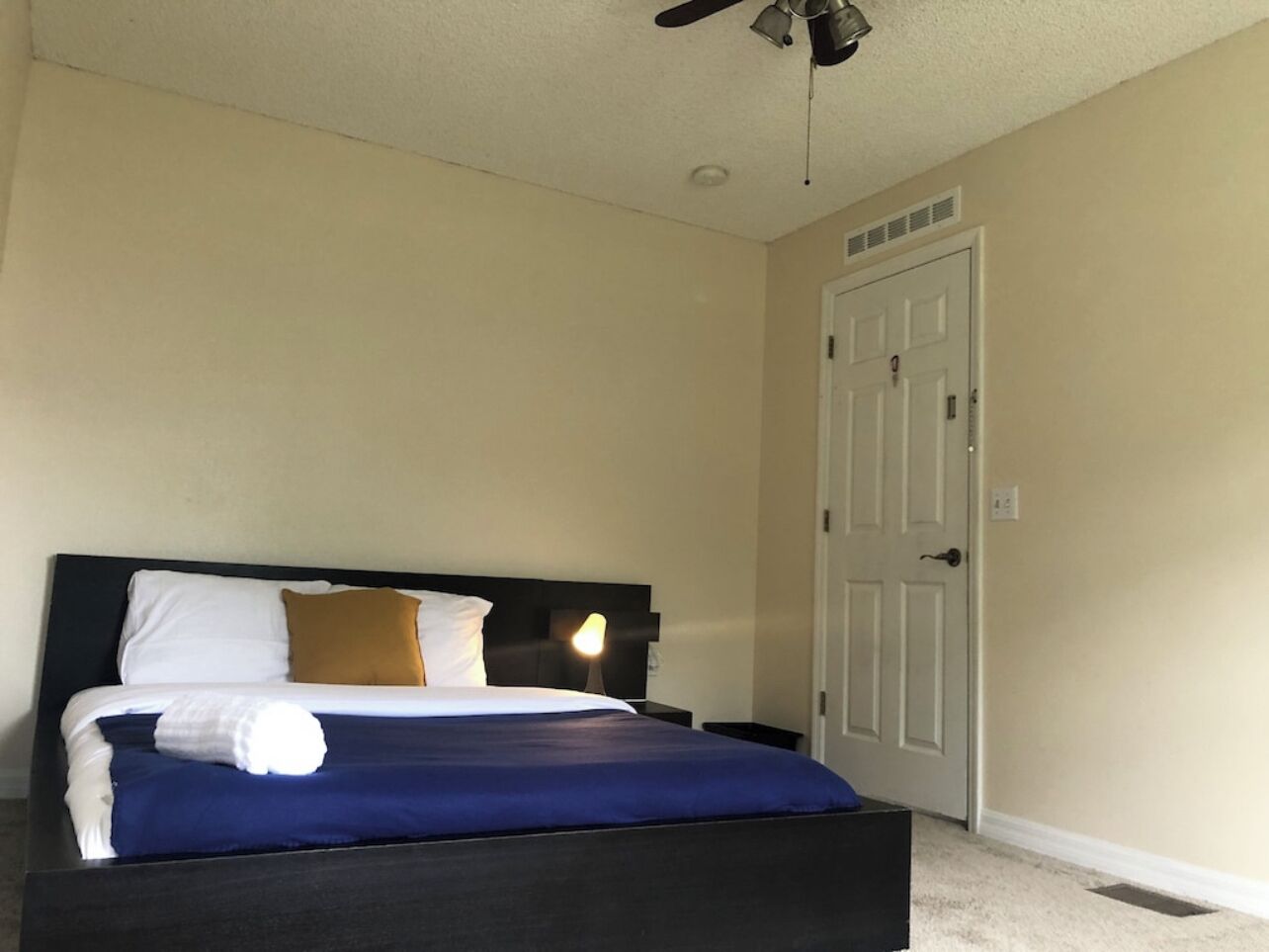 Un dormitorio con cama, mesita de noche, ventilador de techo y puerta.