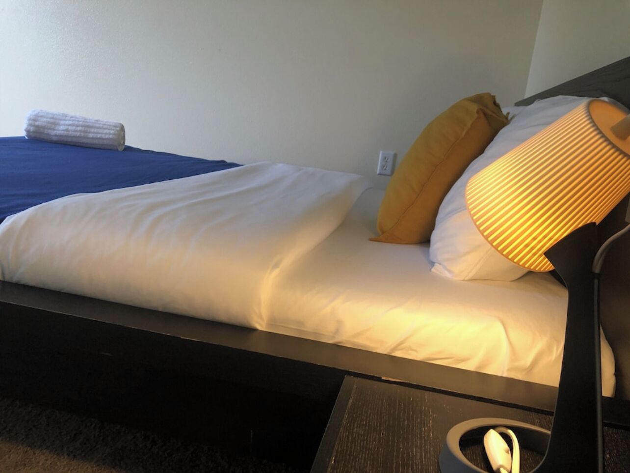 A bed with white and blue bedding, a yellow pillow, and a bedside lamp.