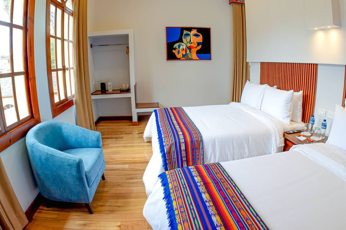 Een hotelkamer met twee bedden, een blauwe fauteuil, een kledingkast en een schilderij aan de muur.