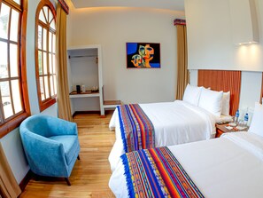 Habitación de hotel con dos camas, un sillón azul, un armario y un cuadro en la pared.