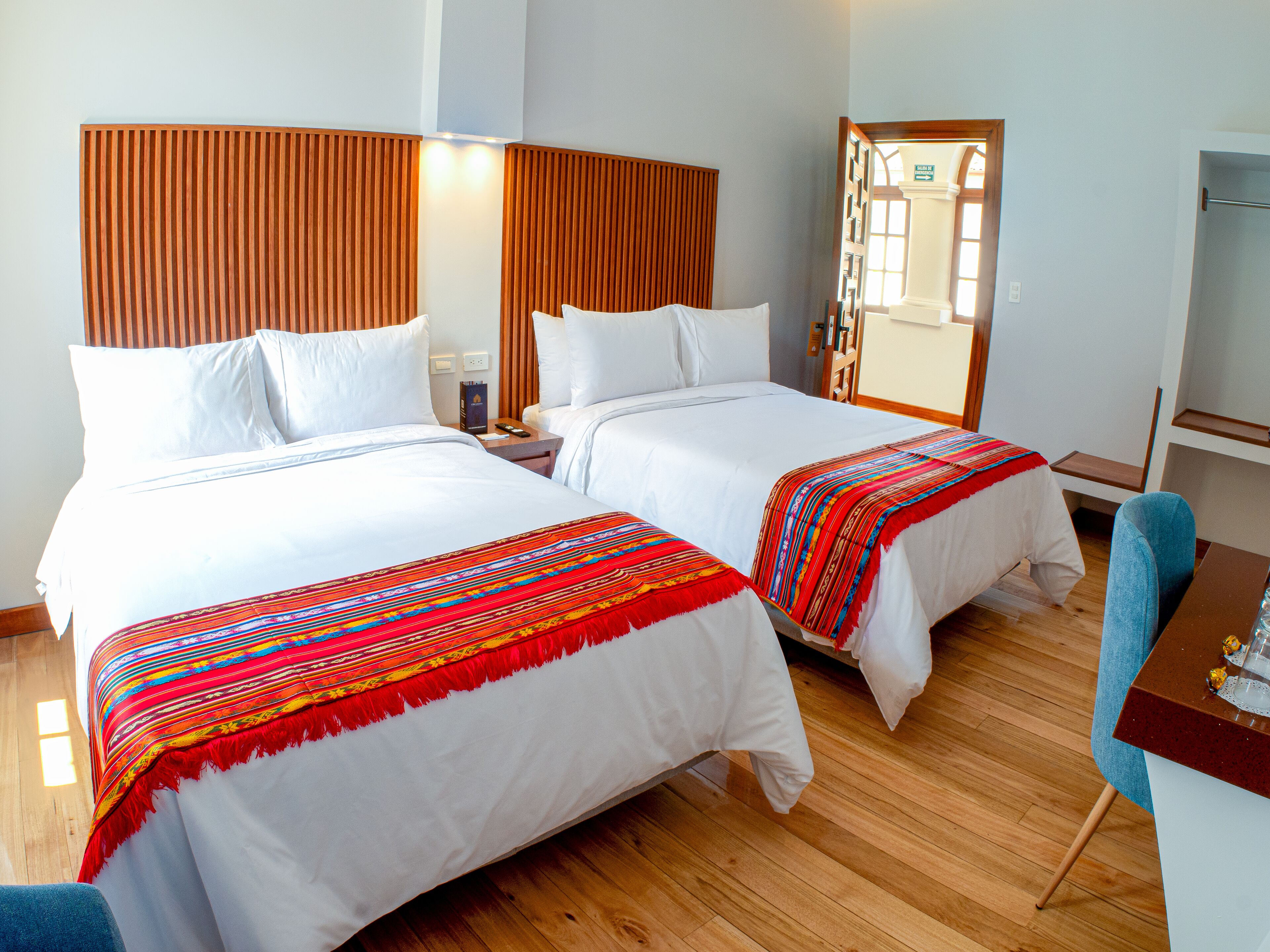 A hotel room with two beds, wooden headboards, white bedding, and a wooden floor.