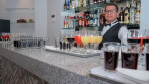 Zona de bar con un cantinero, varias botellas de licores y distintos vasos con bebidas.