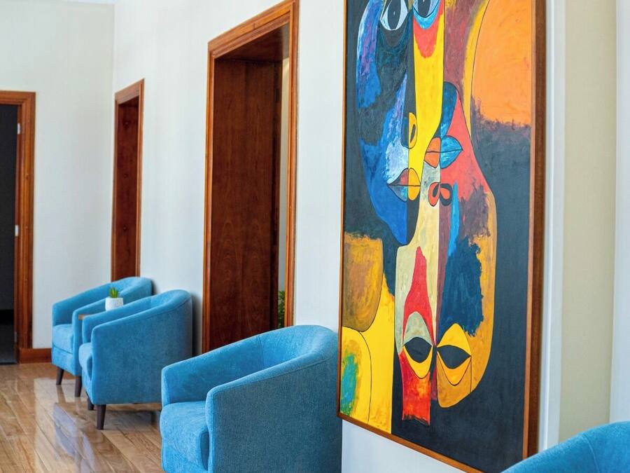 Un vestíbulo de hotel con sillones azules, puertas de madera y un cuadro abstracto grande en la pared.