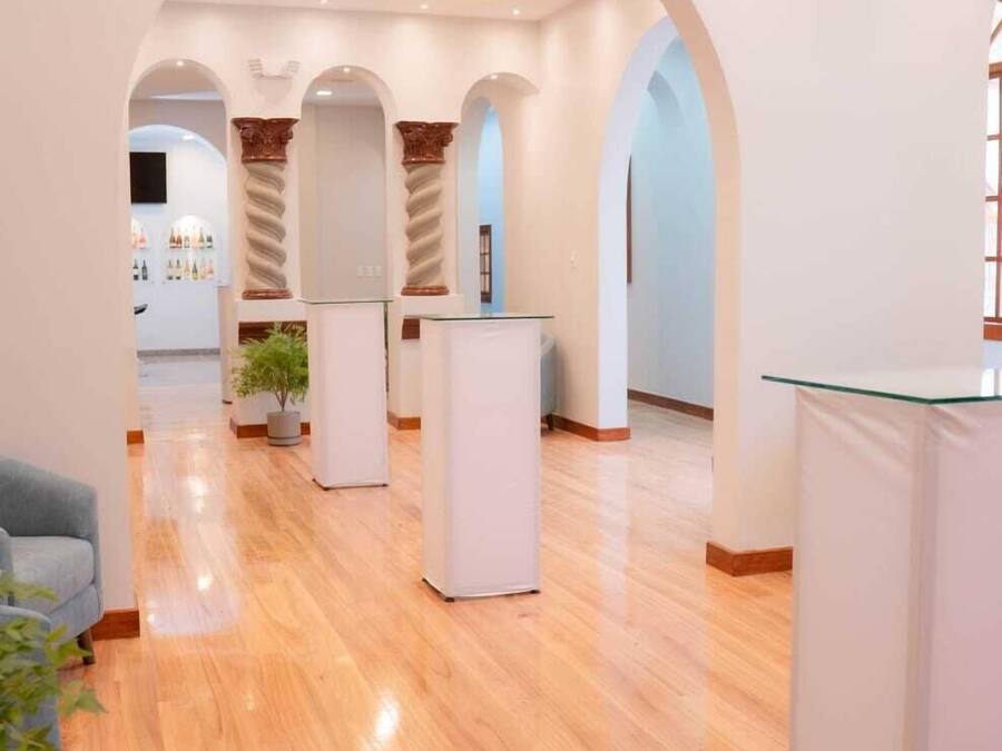 A spacious lobby with wooden flooring, white pillars, and a glass reception desk.