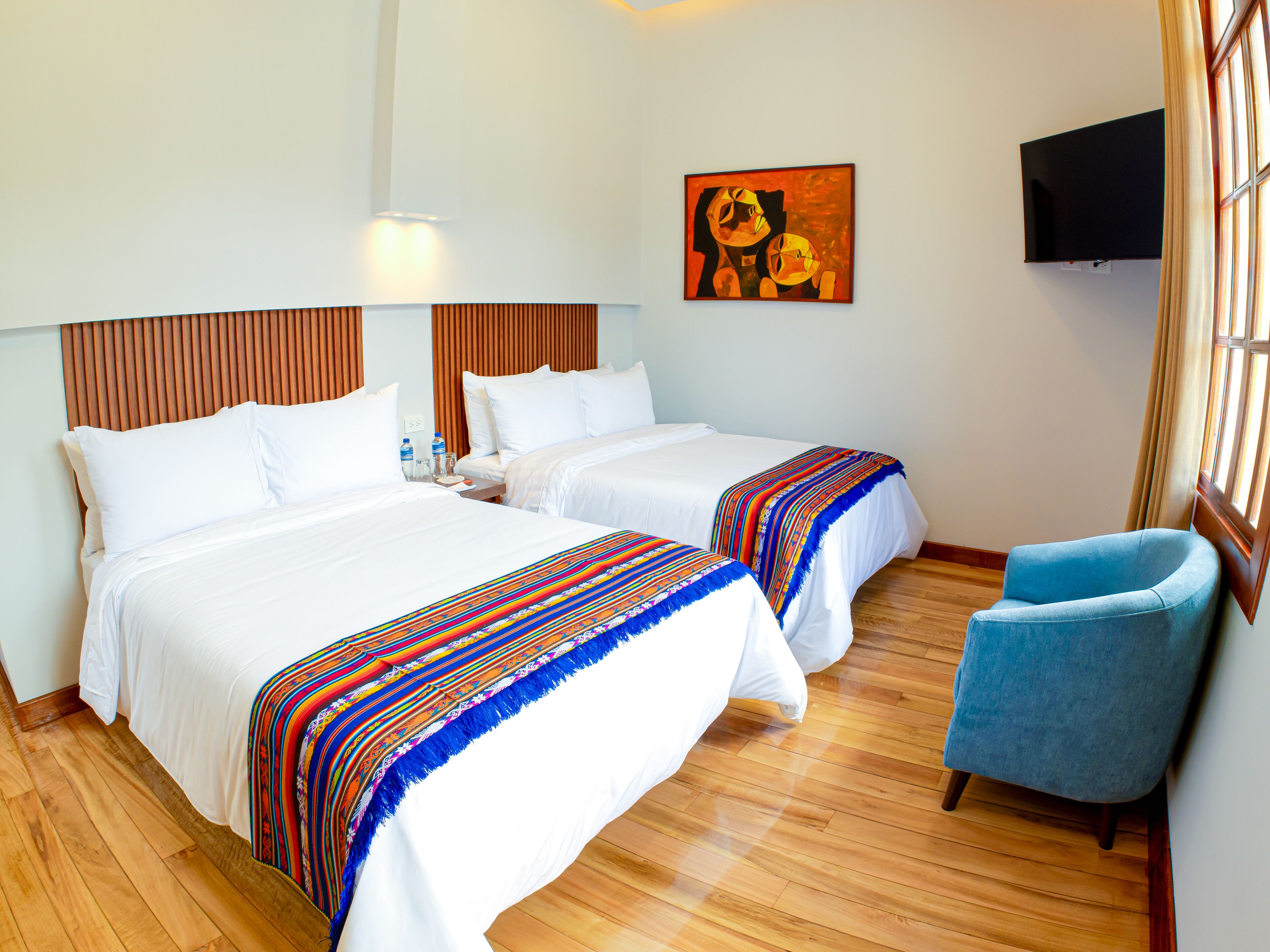 A hotel room with two beds, a TV, and a blue armchair.