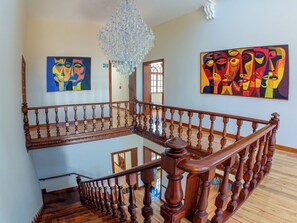 Una escalera de madera con un candelabro, dos cuadros abstractos de colores y una barandilla de madera.