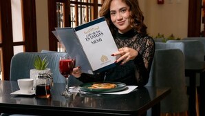Una persona sosteniendo un menú en una mesa, con una bebida y un plato de comida.