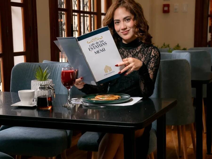 Iemand houdt een menukaart vast aan een tafel, met een drankje en een bord eten.