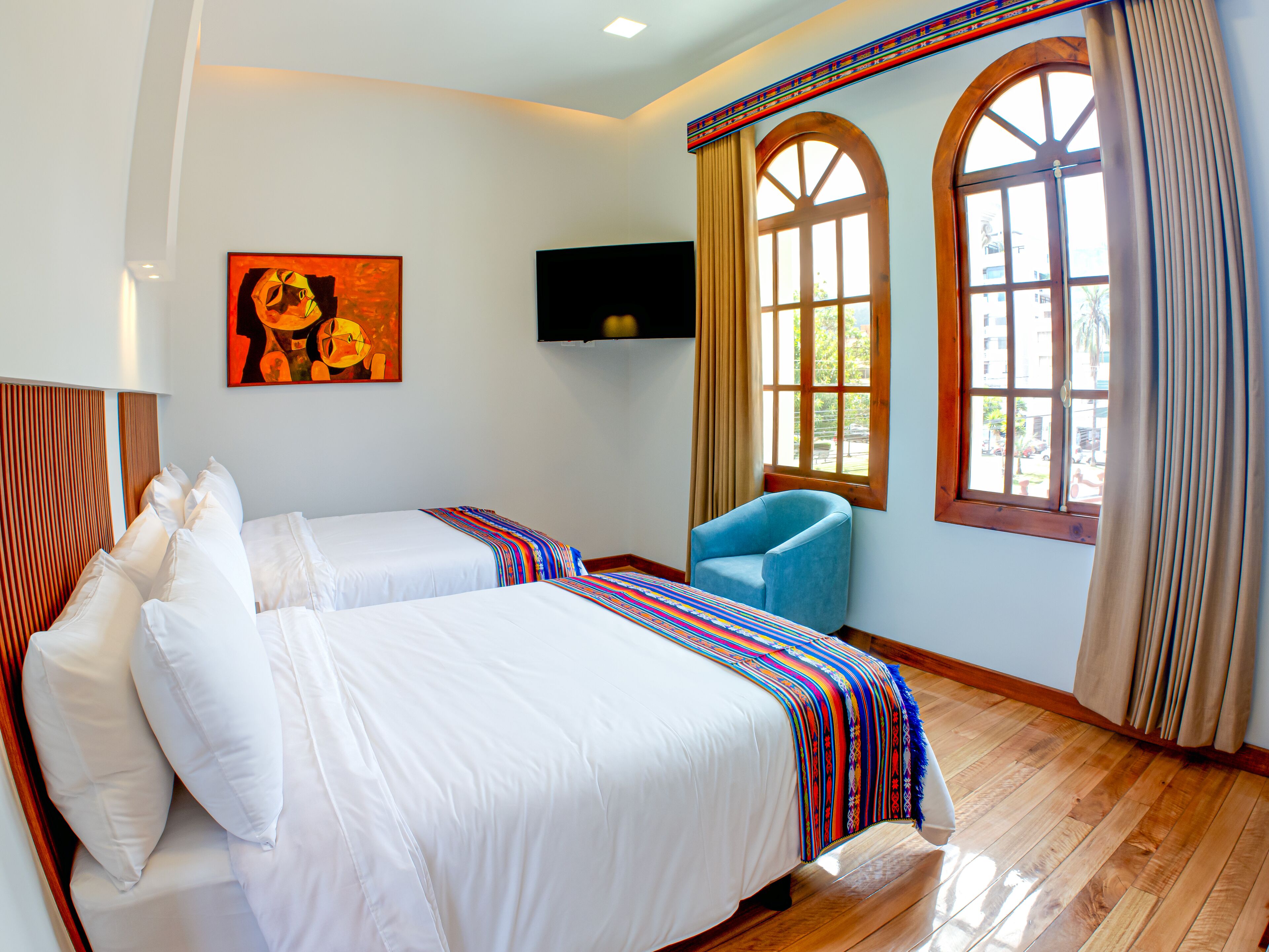A hotel room with two beds, a TV, and large windows with curtains.