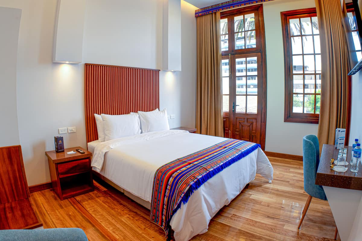 Hotelkamer met een groot bed, houten vloer, een bureau met stoel en een raam met gordijnen.