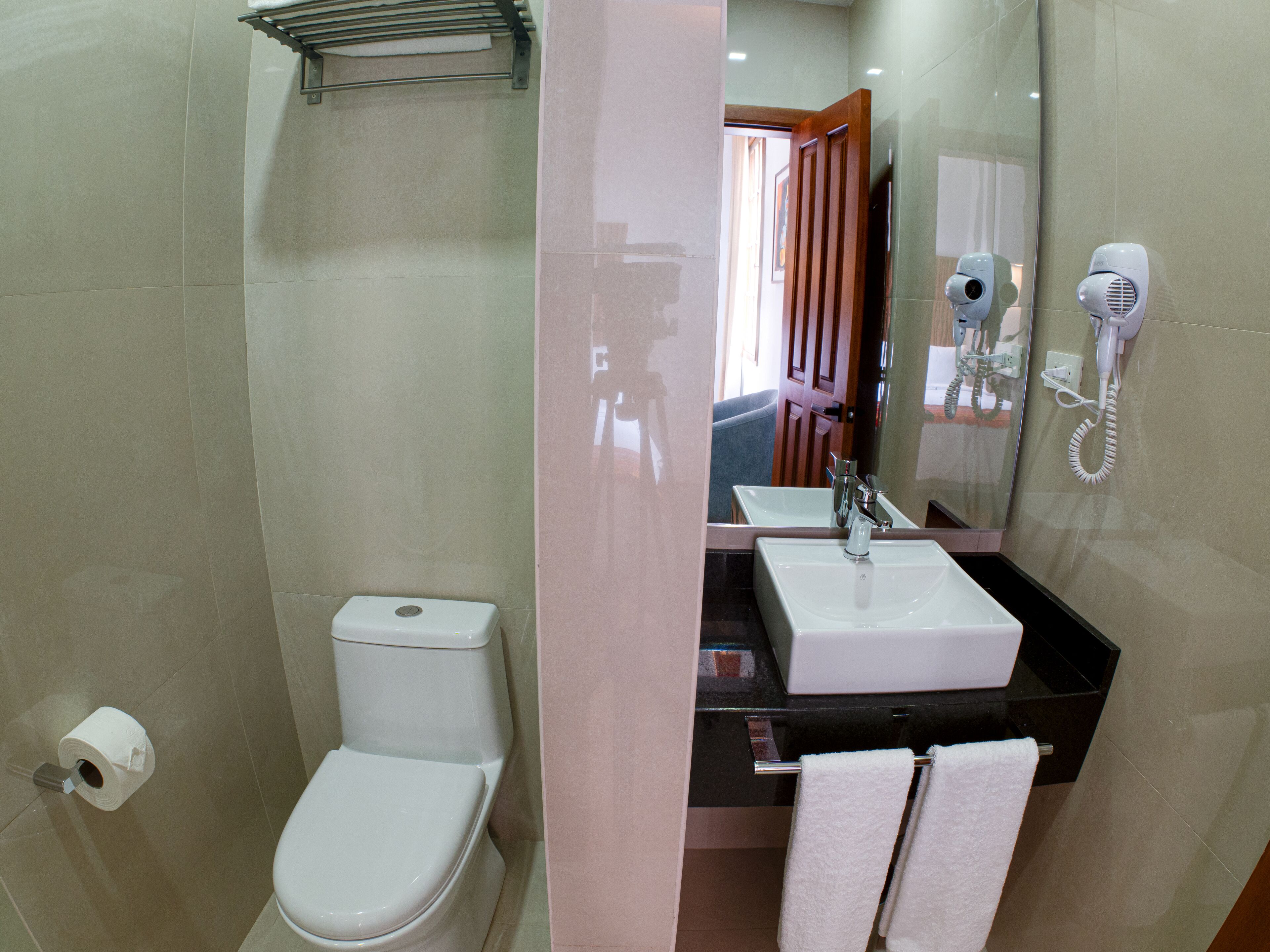 Un baño con inodoro, lavamanos y un secador de pelo en la pared.