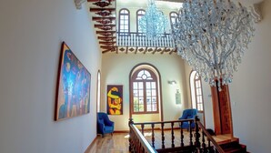 Un interior espacioso con una escalera de madera, una gran lámpara de araña y obras de arte en las paredes.