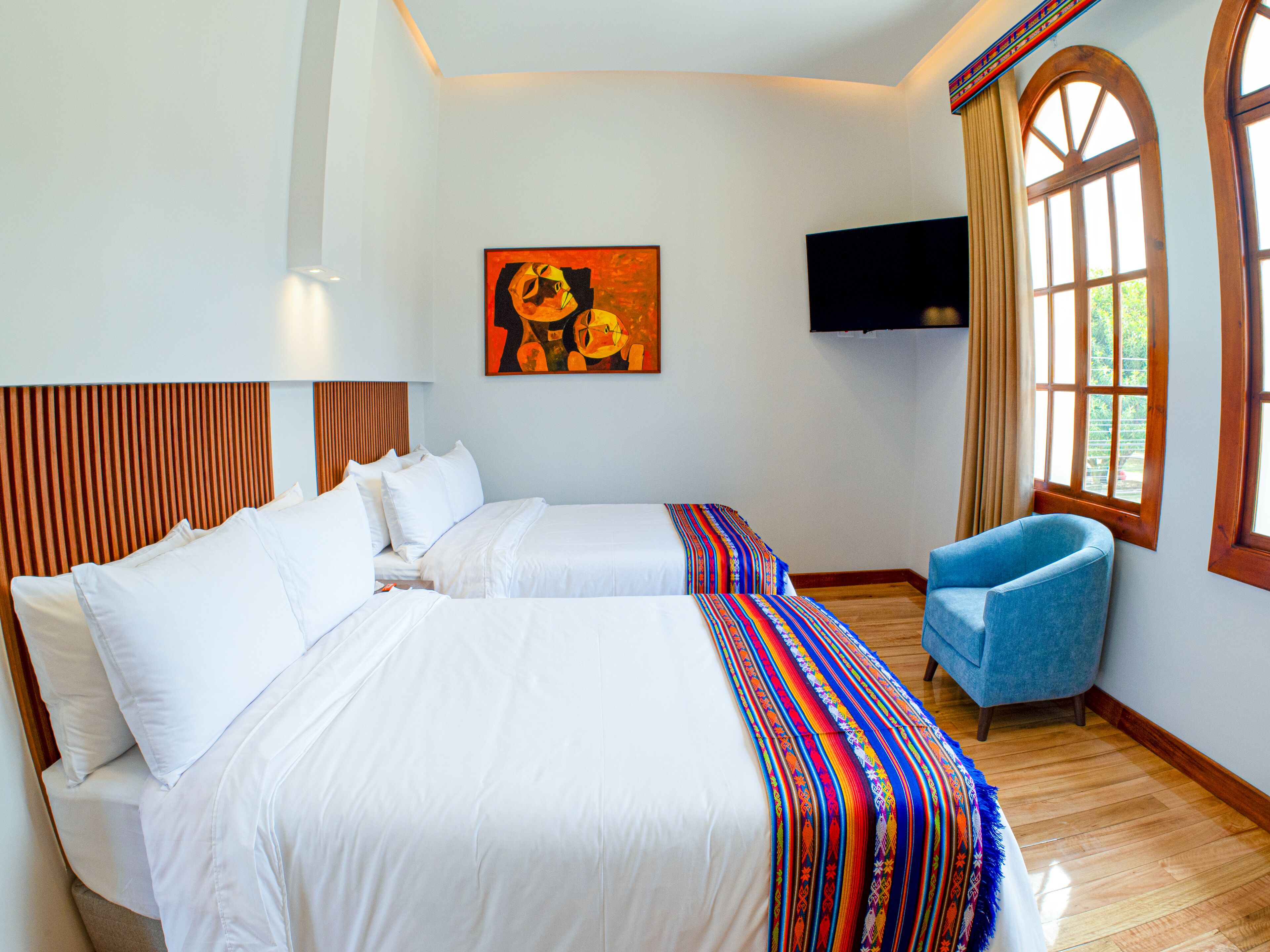 Une chambre d’hôtel avec deux lits, une télévision, une fenêtre avec des rideaux et une chaise bleue.