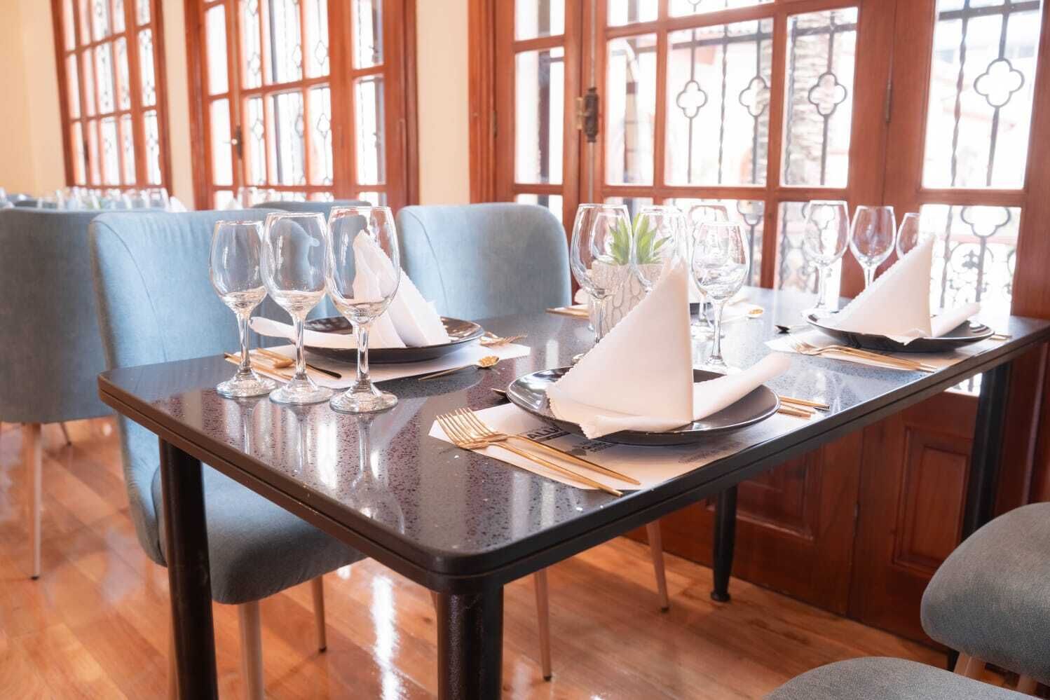 A dining table set with wine glasses, plates, and cutlery, with chairs around it.