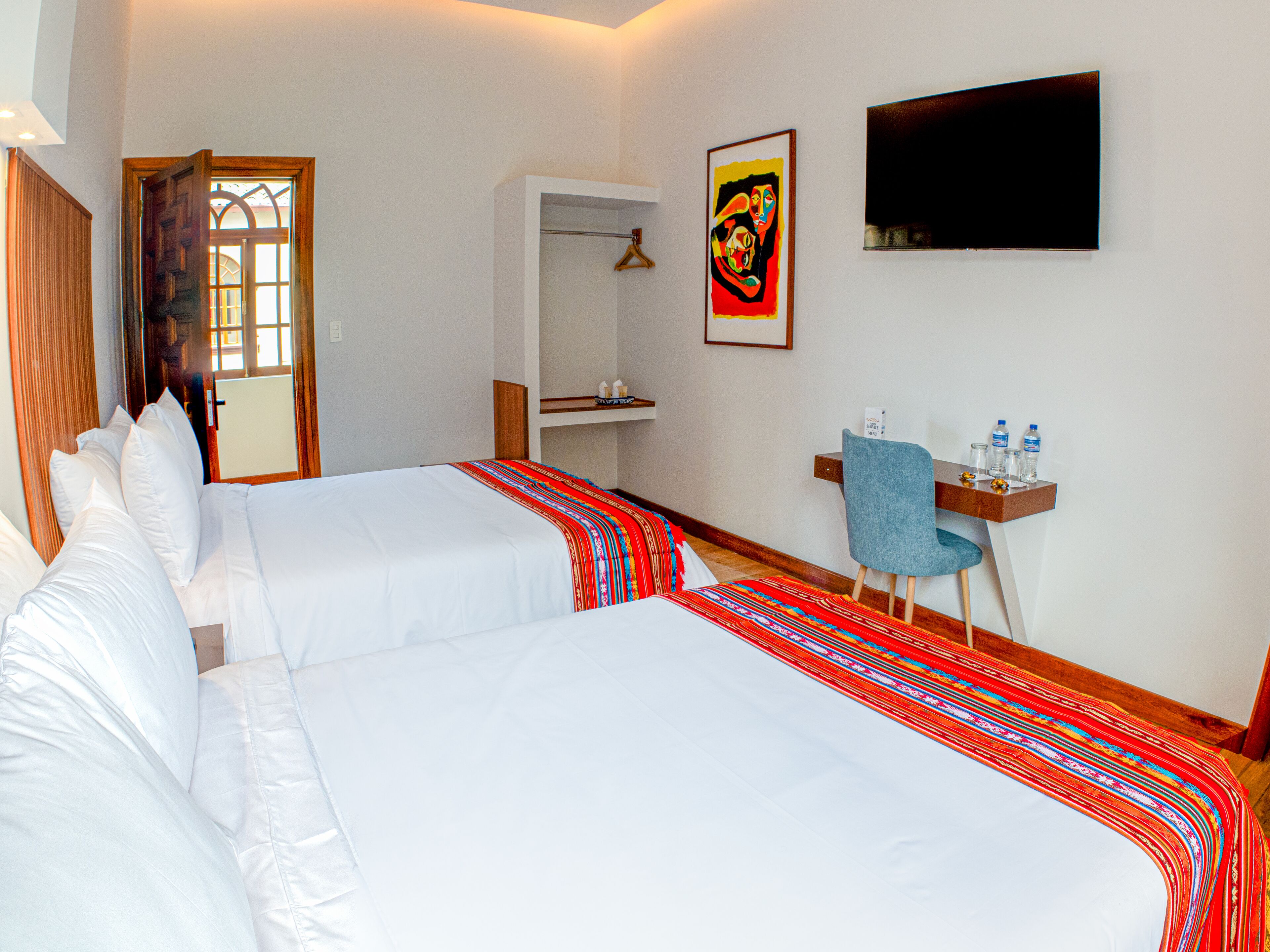 Habitación de hotel con dos camas, un escritorio con una silla, un televisor y un espejo.