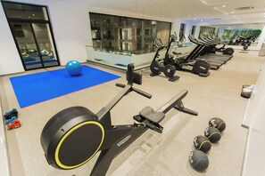 Ein Fitnessraum mit Trainingsgeräten, einer blauen Matte und Kurzhanteln.