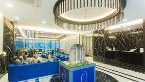 En modern entréhall med en blå möblerad sittgrupp, en modell av en byggnad och en receptionsdisk.