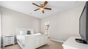 Ein Schlafzimmer mit Bett, Nachttisch, Schminktisch, Deckenventilator und Fernseher.