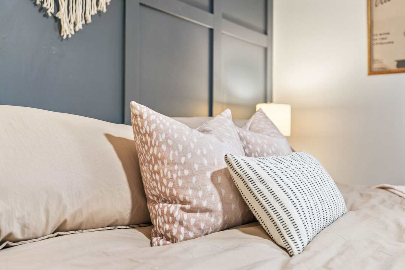Ein Bett mit einem weißen und gemusterten Kissen, einem gestreiften Kissen und einer Wand mit einem gerahmten Bild.